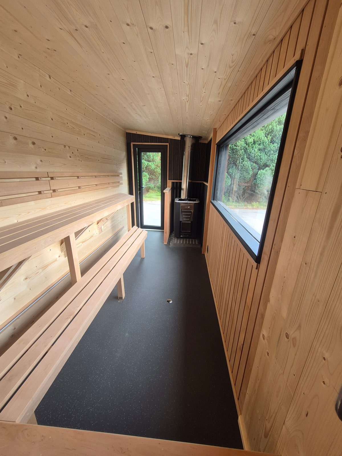 Full Atlantic mobile sauna interior with long two-tier benches, panoramic window and Harvia wood-burning stove