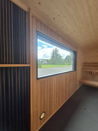 Atlantic mobile sauna interior with panoramic window and heat-shielded wood-burning stove area
